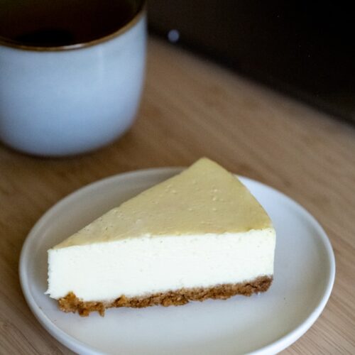 a piece of cheesecake on a plate next to a cup of tea